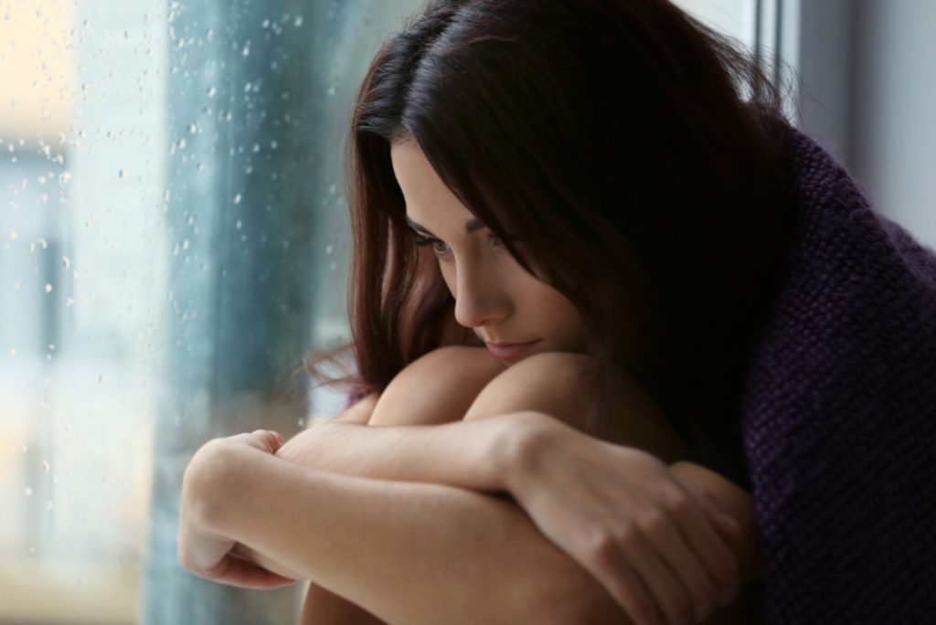 Deprimeret ung kvinde sidder nær vinduet derhjemme