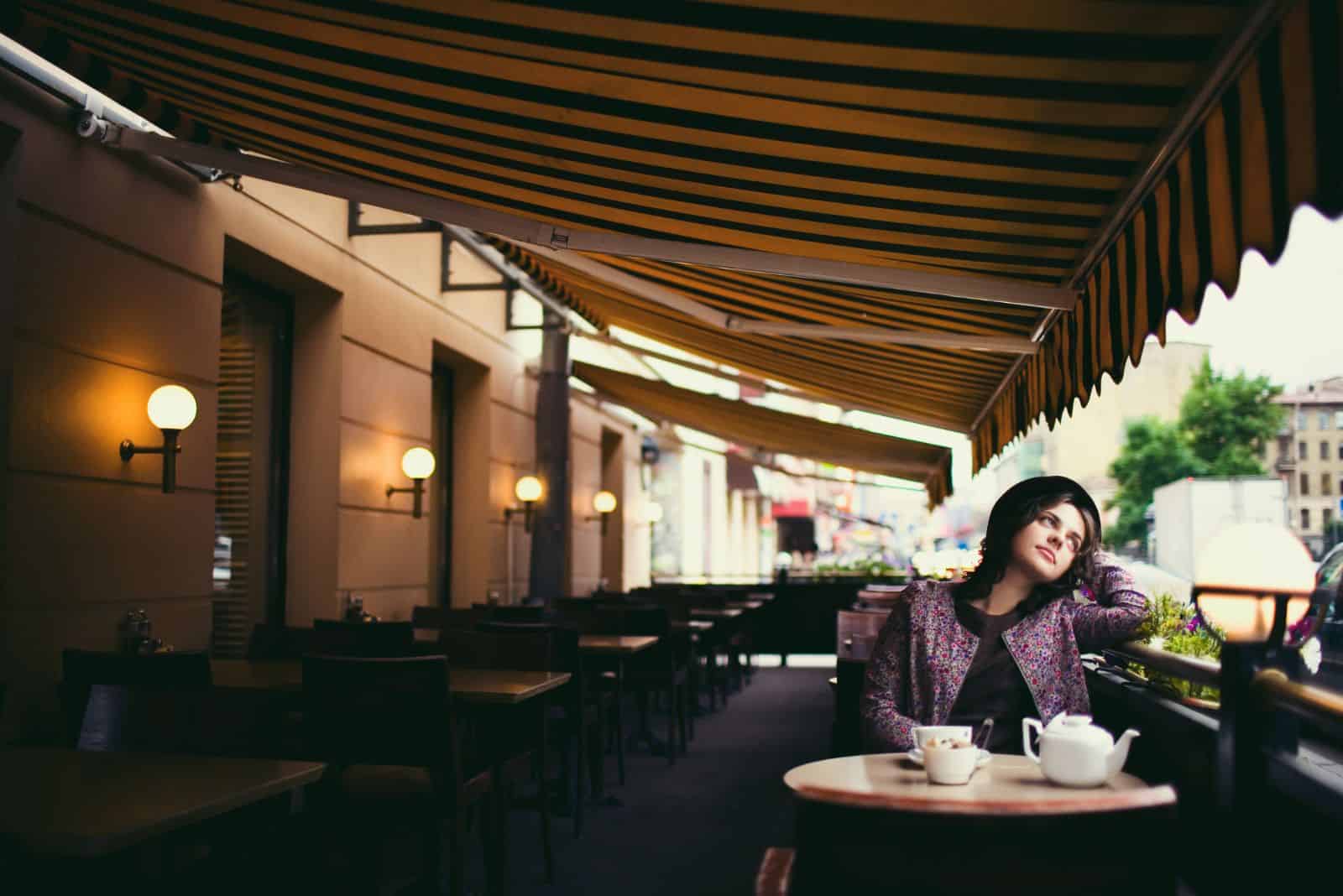 en fundersam tjej med hatt på huvudet sitter på ett kafé