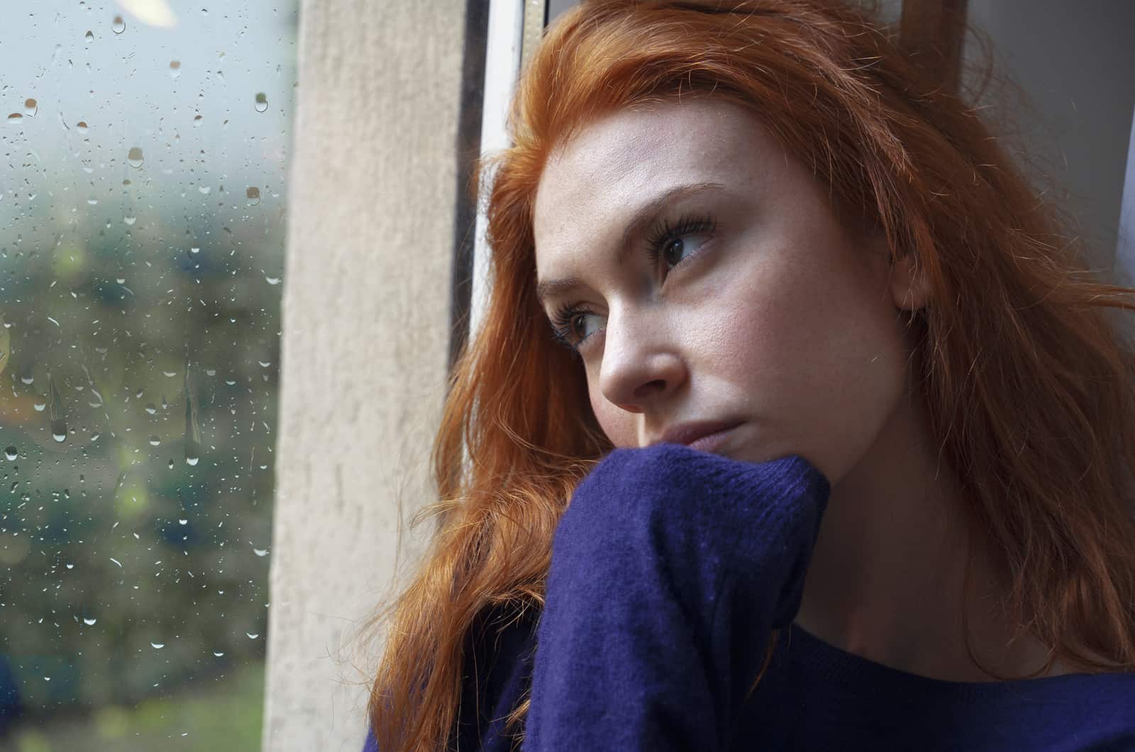trist rødhåret kvinde ser uden for vinduet