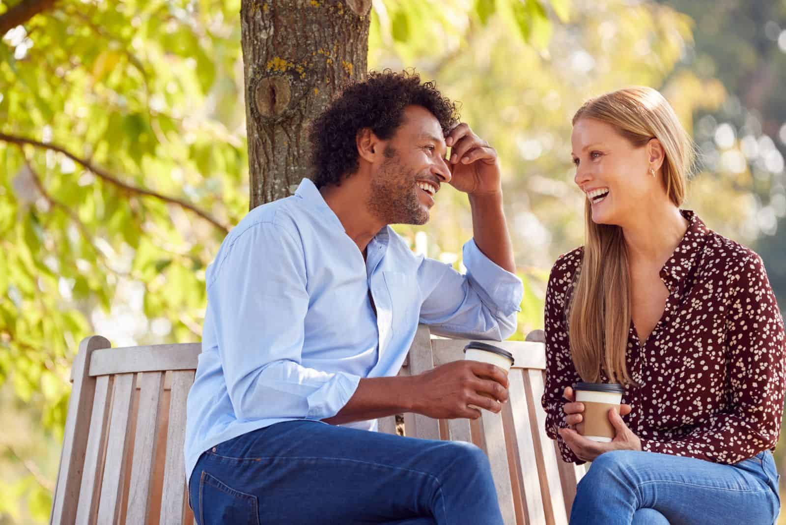 leende älskande par sitter i parken och pratar över kaffe