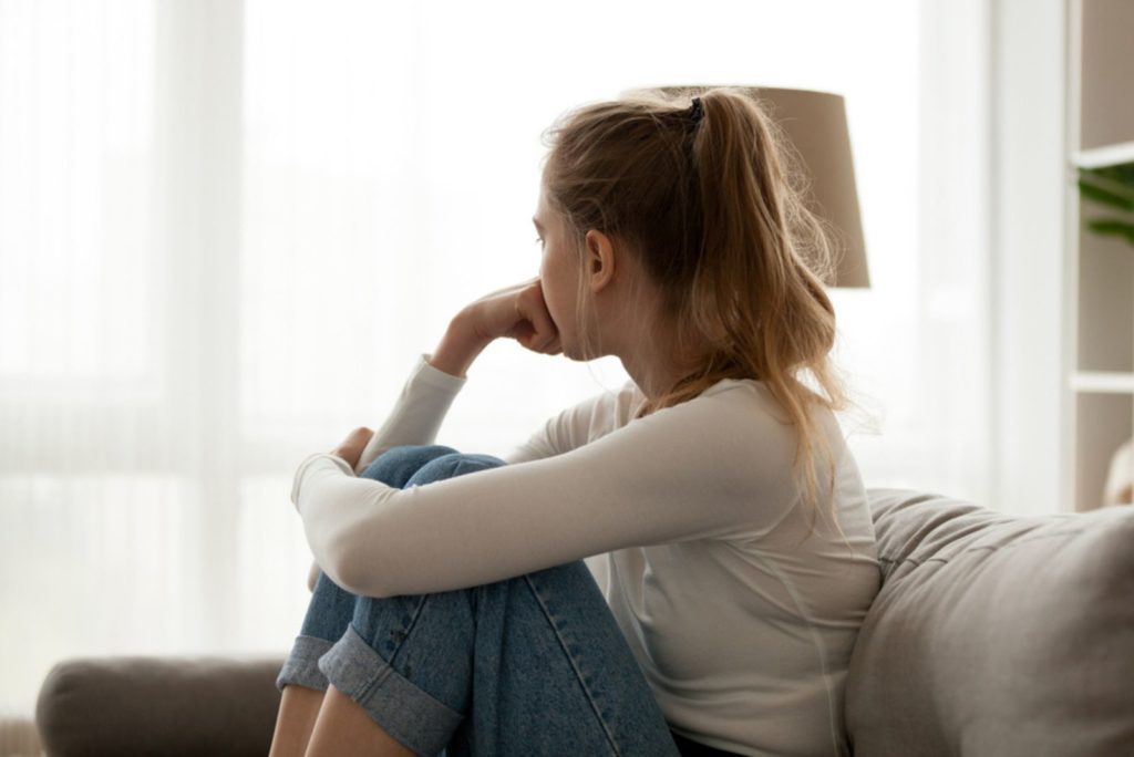 ung kvinde kigger væk på vinduet sidder på sofaen