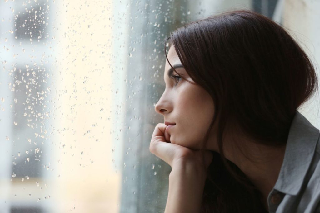 Deprimeret ung kvinde nær vinduet derhjemme