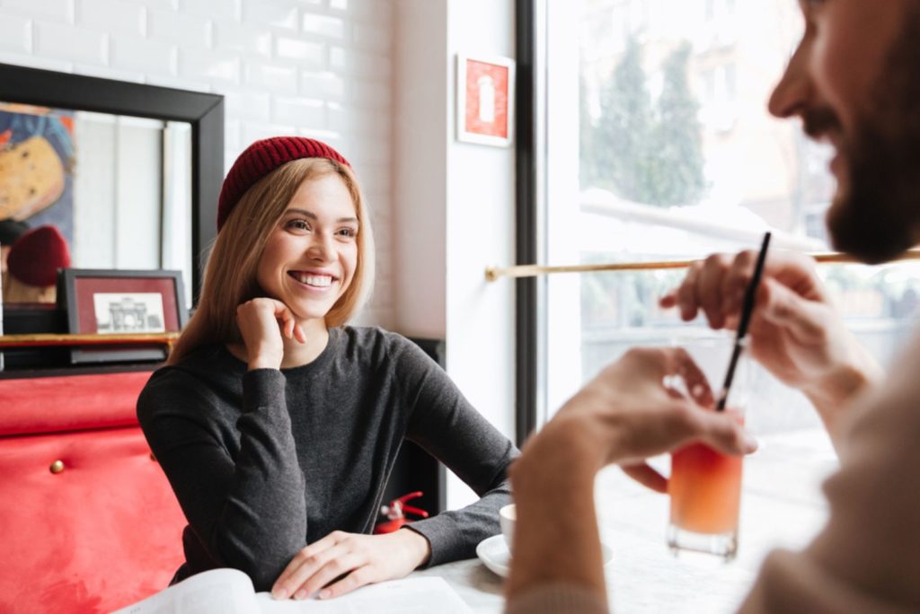 Smilende kvinde i rød hat taler med mand ved bordet i cafeen