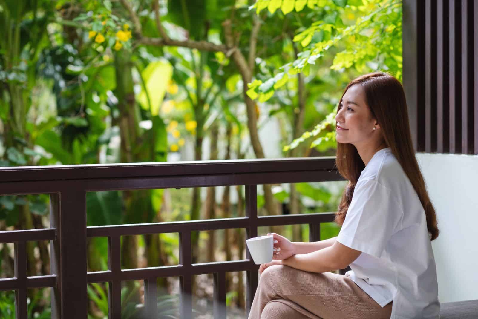 en vakker jente sitter på balkongen og drikker kaffe