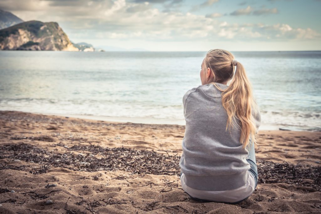 Eftertænksom ensom ung kvinde sidder på stranden og krammer knæene