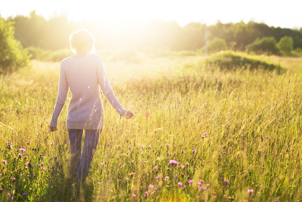 Ung kvinde, der går i marken mod solen, der holder en valmueblomst