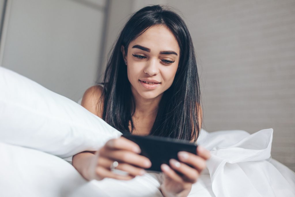kvinde, der bruger smartphone, mens hun ligger på sin seng