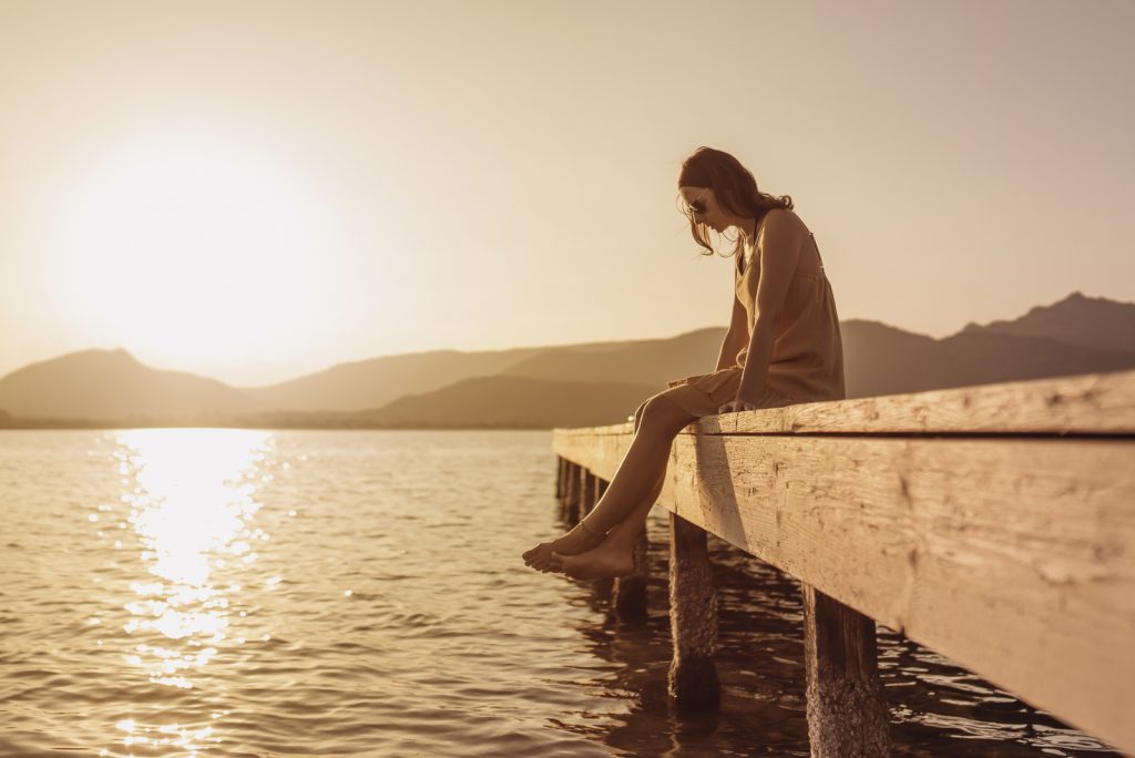 kvinde sidder på en mole ved en sø og ser ned til vandet ved solnedgang