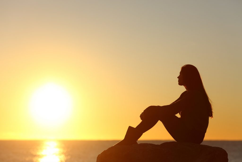 kvinde silhuet ser solen på stranden ved solnedgang