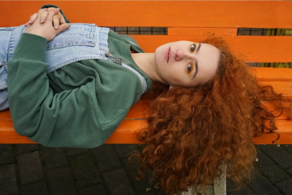 rødhåret kvinde liggende på orange bænk i solrig efterårsdag