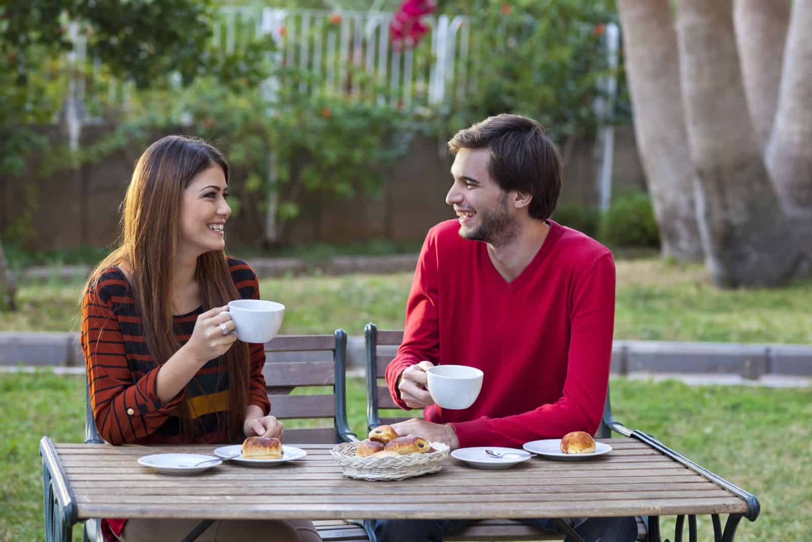 en mann og en kvinne sitter utendørs og snakker over frokosten