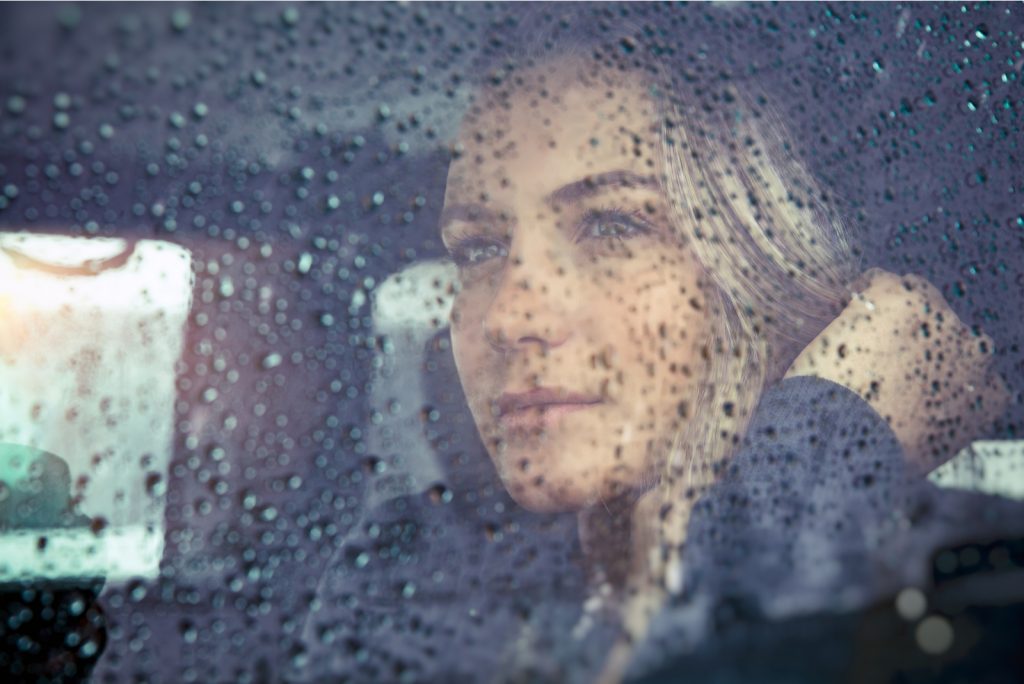 smuk trist kvinde sidder i bilen i regnvejr